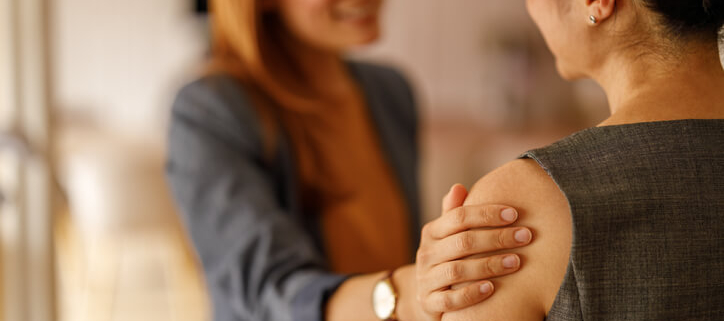 Two women facing each other. One woman reassures the other with her hand on her arm.a