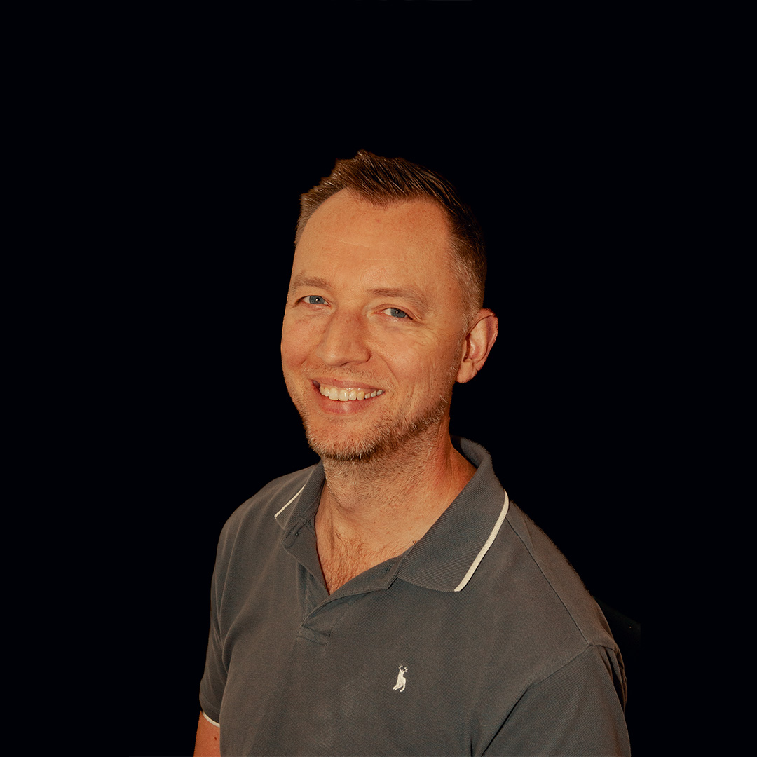 Picture of a smiling man from the shoulders up against a black background