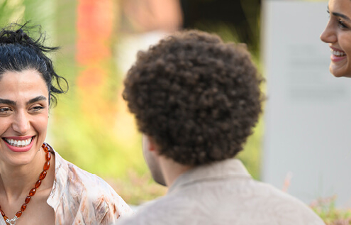 A man and woman in an outdoor setting. The woman is smiling at the man who is faced away from camera.