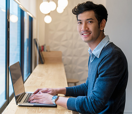Smiling man looking into camera while using laptop