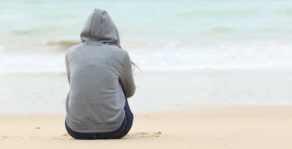 Woman in hoodie sitting on the beach on a winter morning