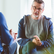 Older man talking to mental health psychologist in brightly lit room