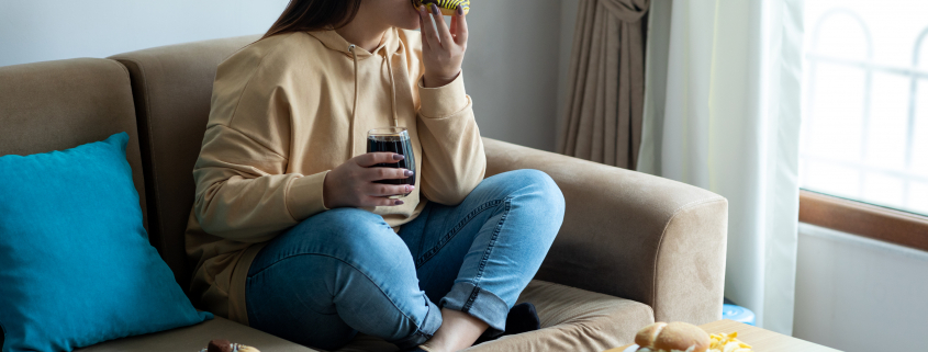 Woman eating sugary food on sofa eating disorders concept image