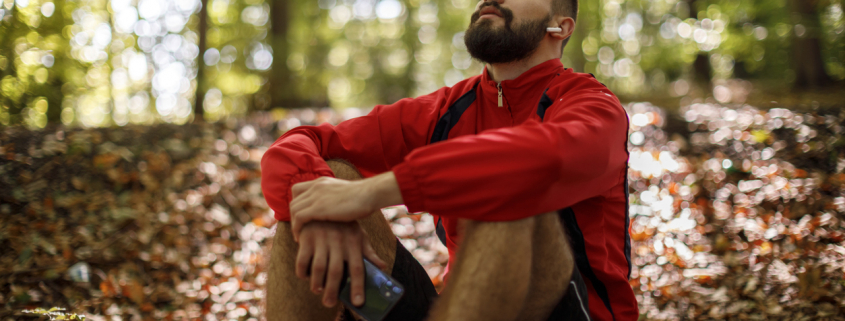 Portrait of relaxed young man with bluetooth headphones in forest