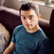 Young down syndrome man sitting on the sofa at home and looking at camera.