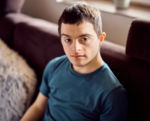 Young down syndrome man sitting on the sofa at home and looking at camera.