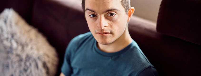 Young down syndrome man sitting on the sofa at home and looking at camera.