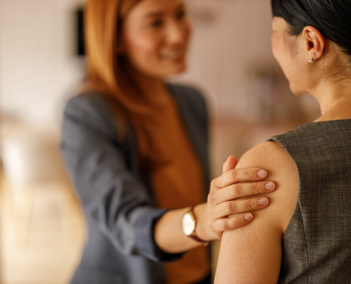 Two women facing each other. One woman reassures the other with her hand on her arm.a
