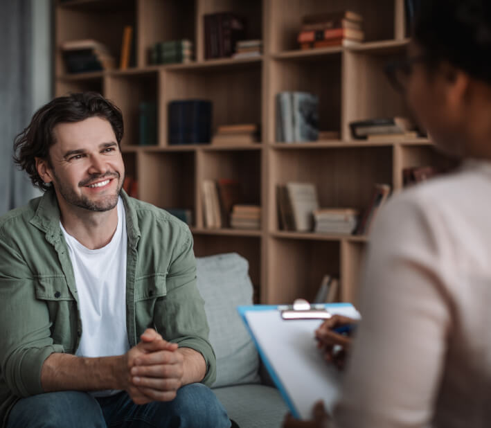 Seated man, smiling at a woman with a clipboard in her hand