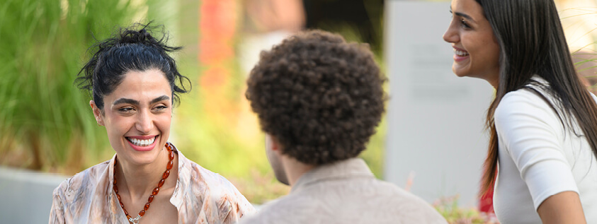 A man and woman in an outdoor setting. The woman is smiling at the man who is faced away from camera.