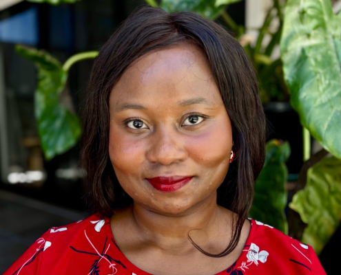 Professional headshop of a woman in a red dress against a leafy background