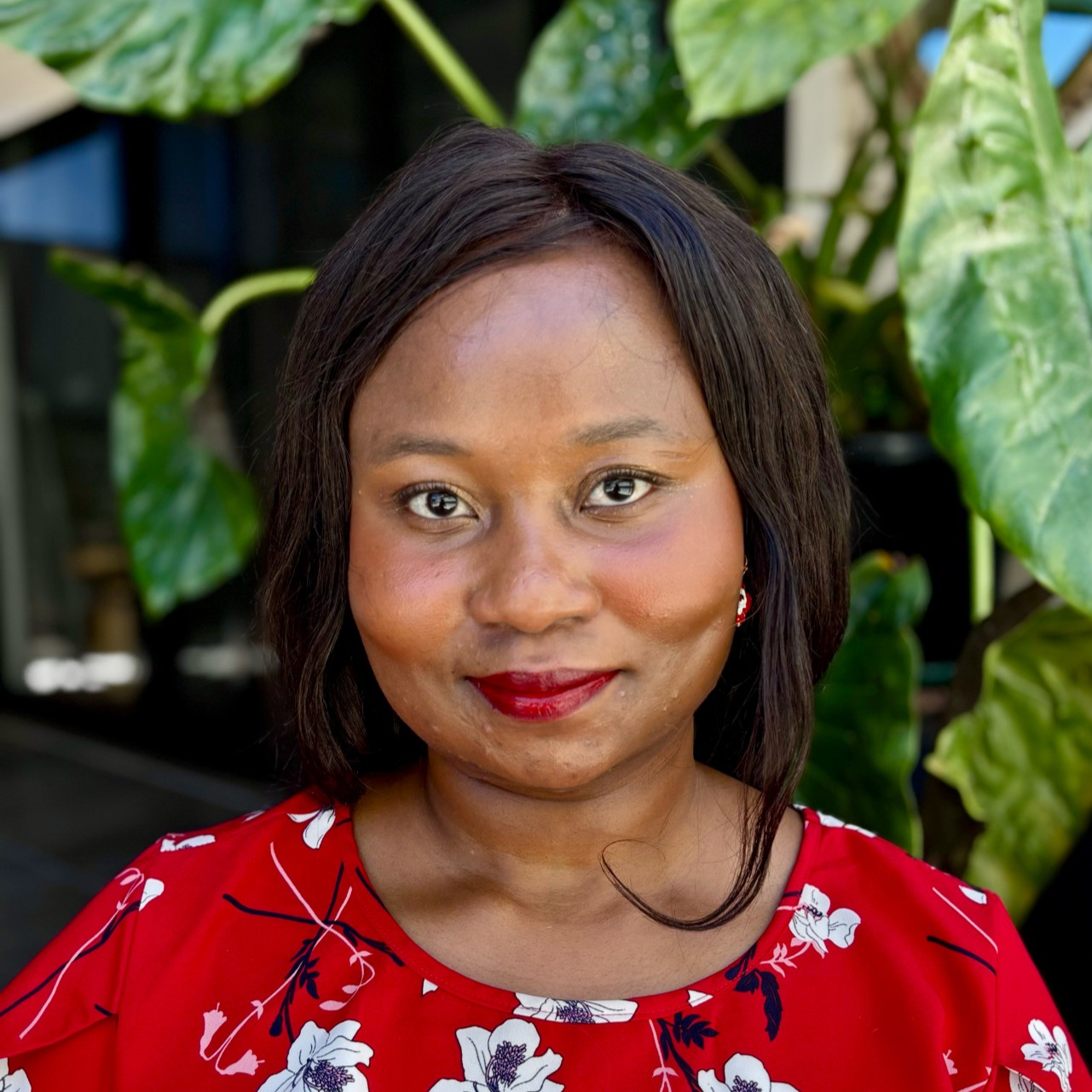 Professional headshop of a woman in a red dress against a leafy background